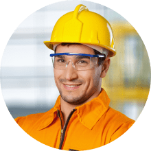 Smiling male construction worker in an orange uniform and yellow hard hat with safety glasses.