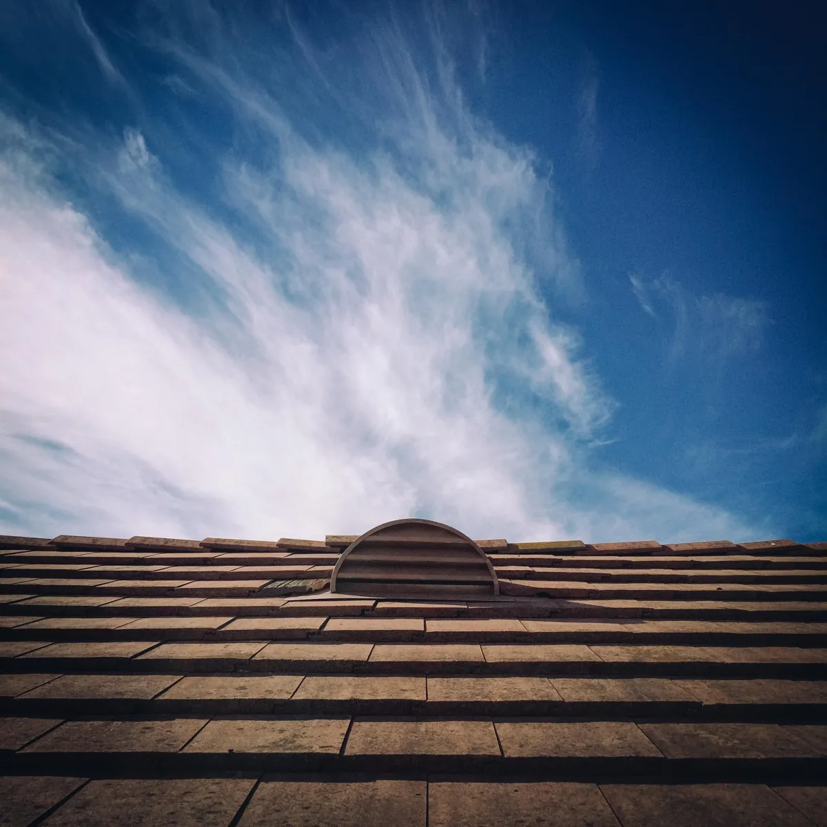 Clay tile roof with a small round vent and dramatic cloudy blue sky.