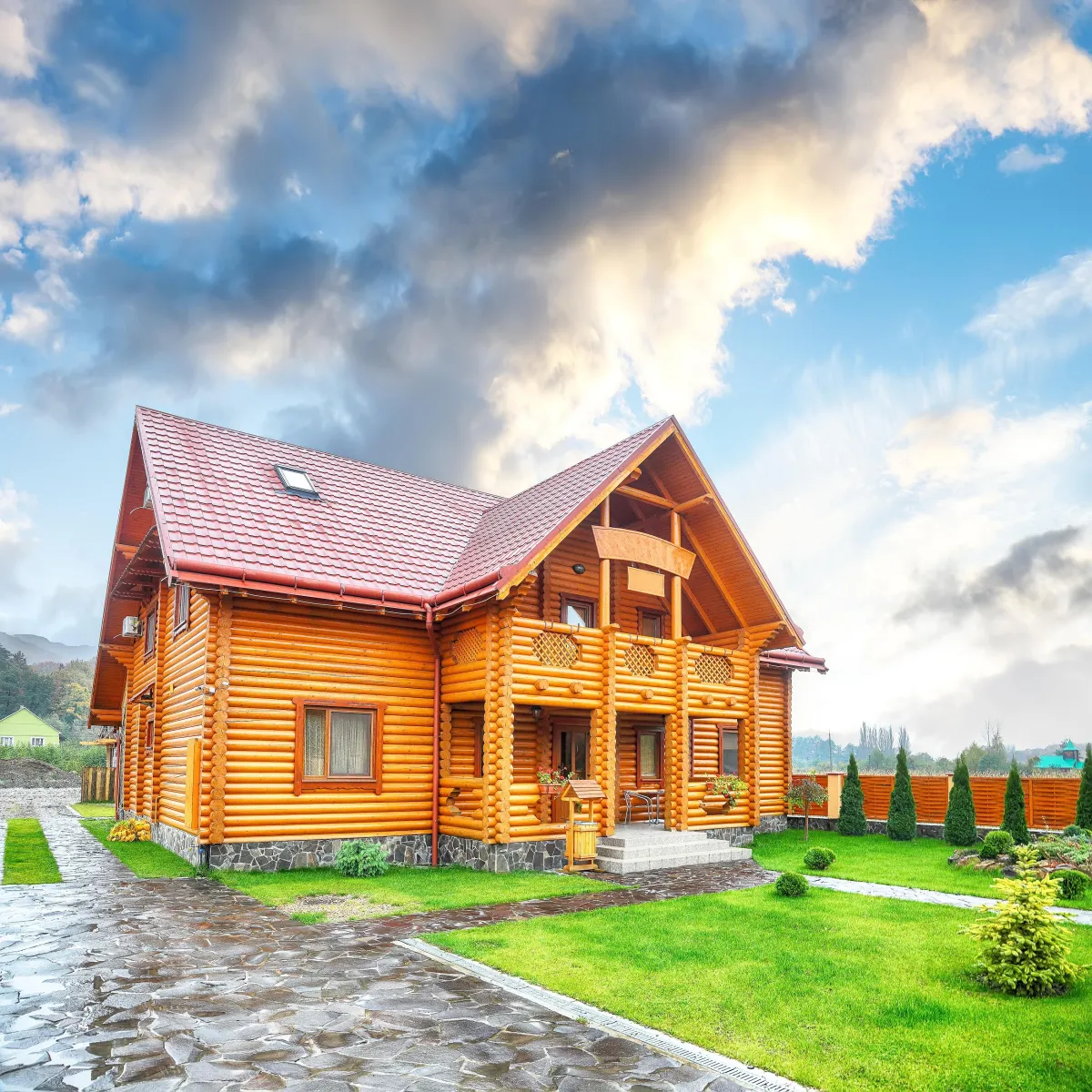 Large wooden log house with red tiled roof in a landscaped yard under cloudy sky.