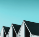 Row of modern houses with steep gabled roofs against a clear blue sky.