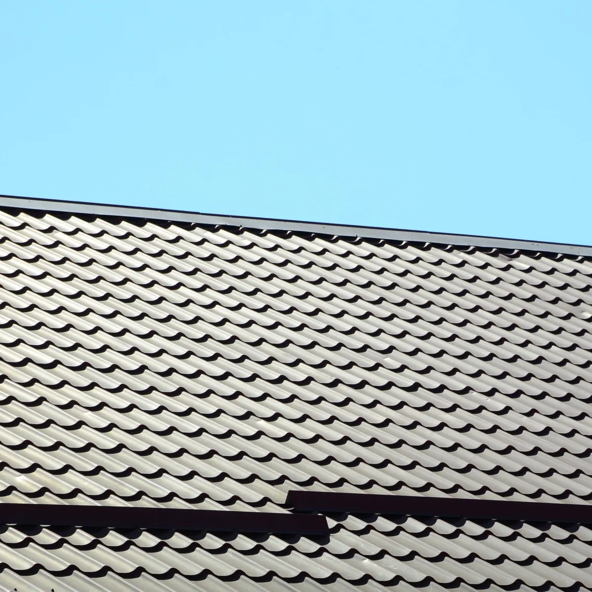 Close-up of a metal tile roof with wavy pattern under clear blue sky.