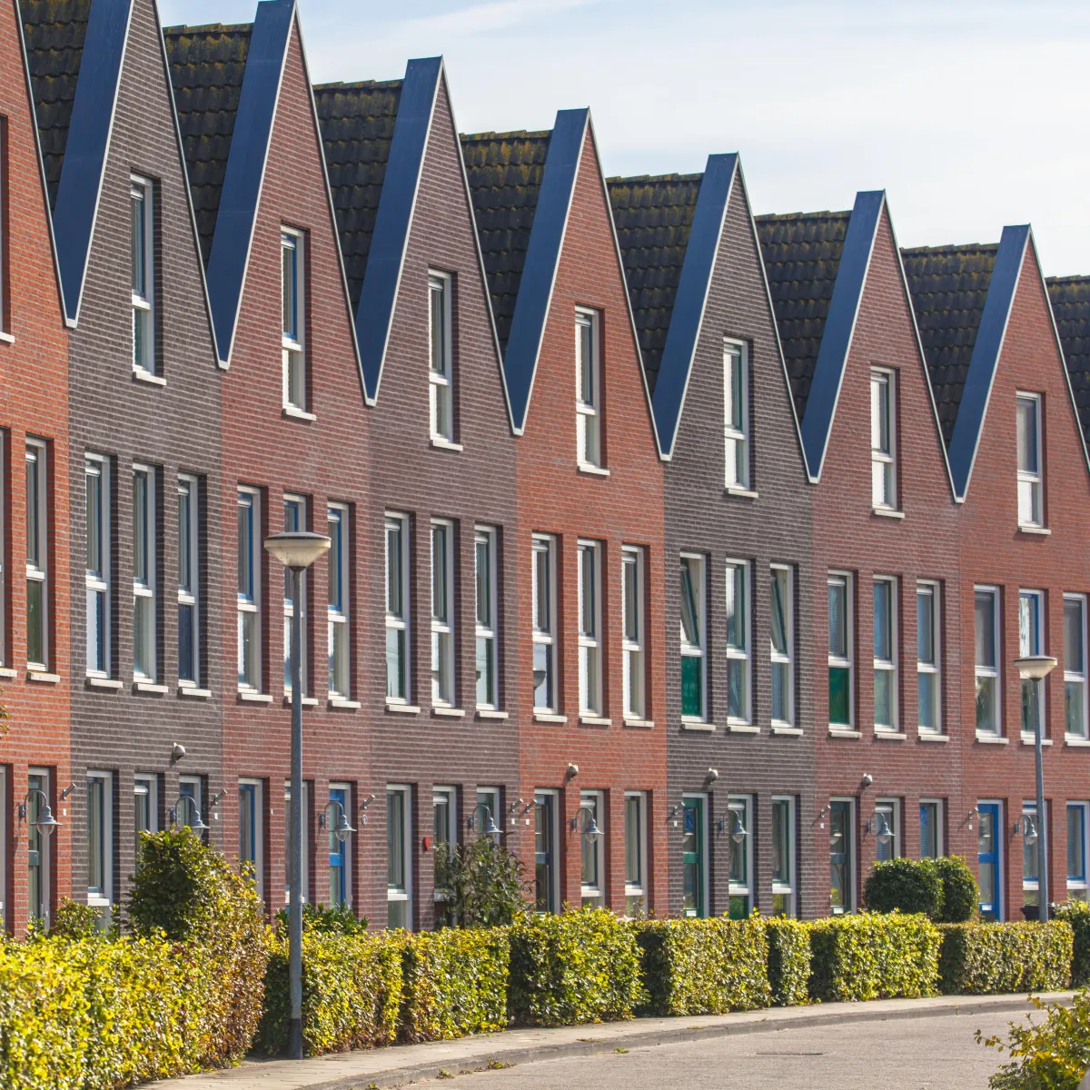 Row of modern townhouses with steep gabled roofs and red and gray brick facades.