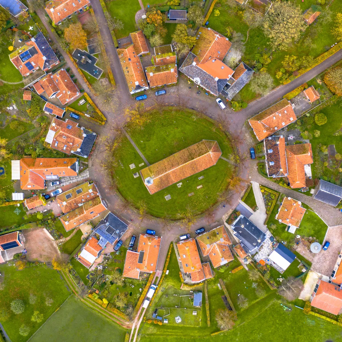 Aerial view of a circular village with orange tiled roofs and green gardens.
