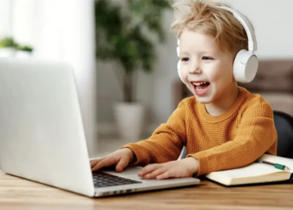 Child with headset smiles as he engages with laptop