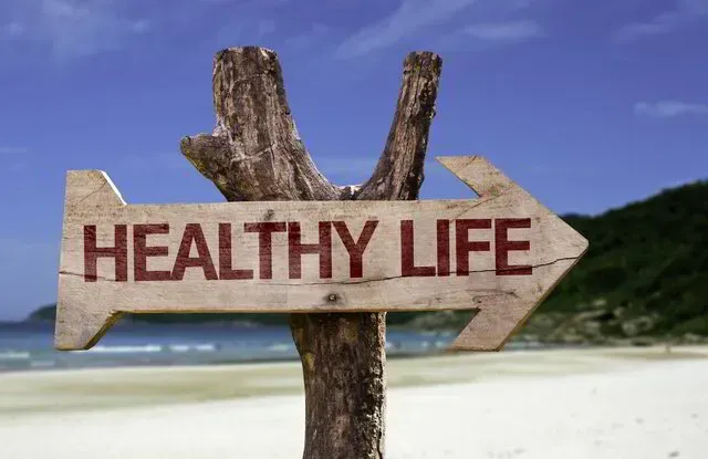Wegweiser mit der Aufschrift 'Healthy Life' an einem sonnigen Strand – Symbol für den Weg zu mehr Gesundheit und ganzheitlichem Wohlbefinden.