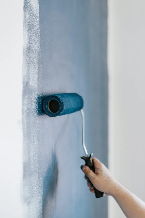 A hand painting the bluew wall using a paint roller