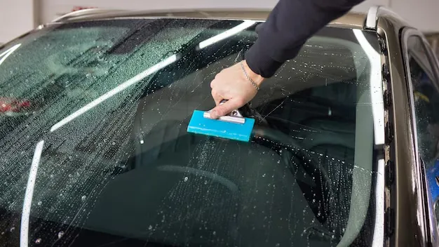 Technician applying premium paint protection film (PPF) to vehicle hood, showcasing expert installation and attention to detail in a professional setting.