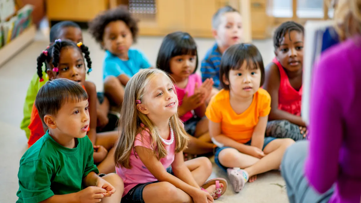 Students sit in a semicircle watching the teacher on a laptop