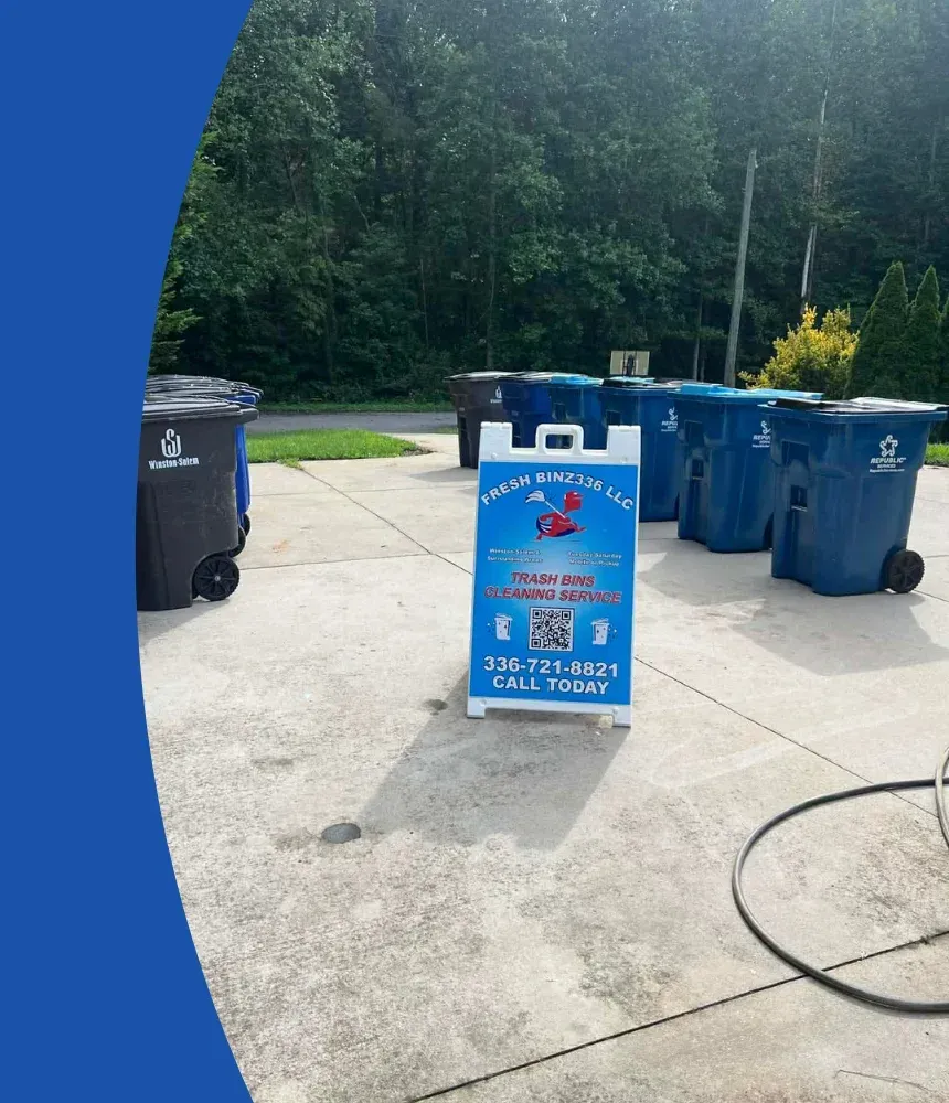 A "Fresh Binz 336 LLC" A-frame sign advertising trash bin cleaning service, surrounded by multiple blue and black bins.