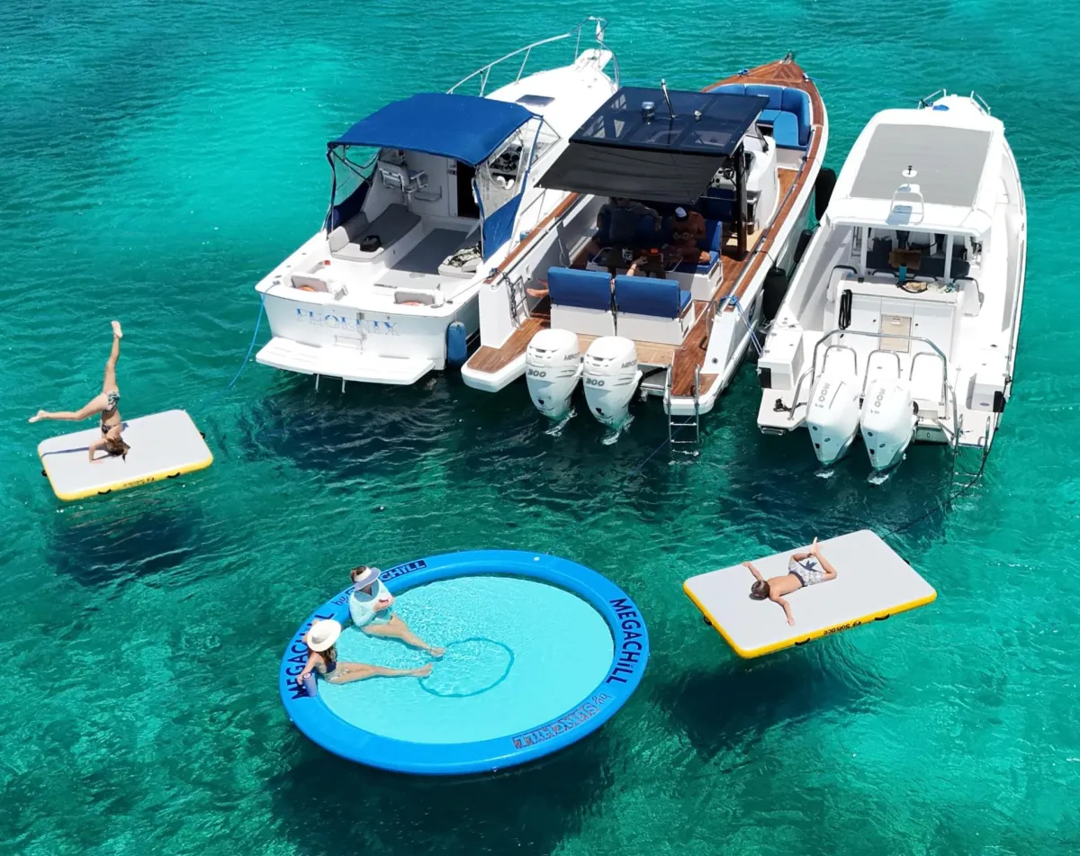 Three charter boats rafted together over turquoise water with floating mats and an inflatable island