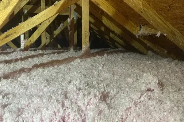 Blown-in attic insulation installed between wooden roof trusses to improve energy efficiency, reduce heat loss, and enhance home comfort.