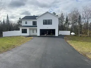 A newly sealcoated driveway in front of a white house in Newport, Maine