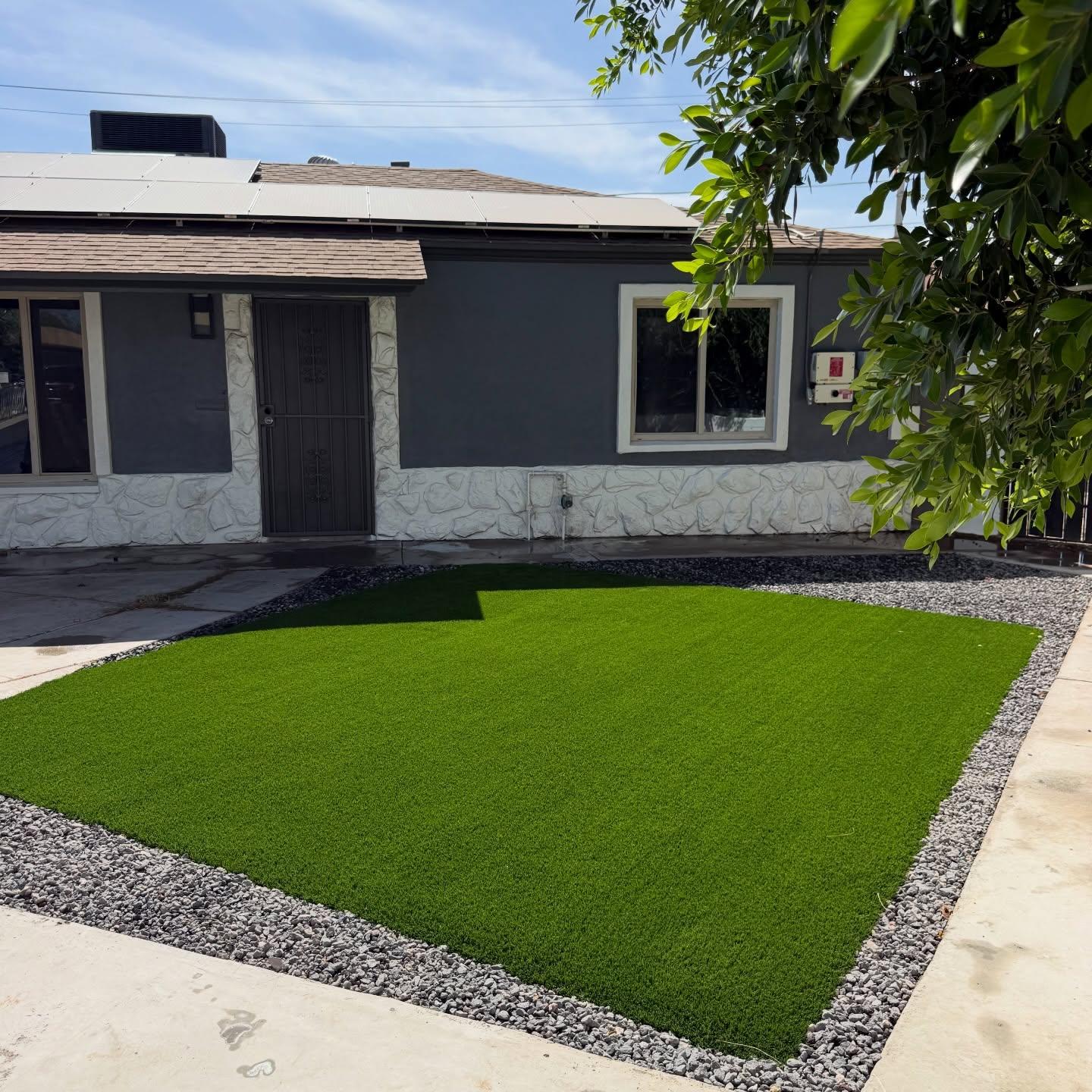 Front-yard artificial turf installation with charcoal stucco and white stacked-stone base