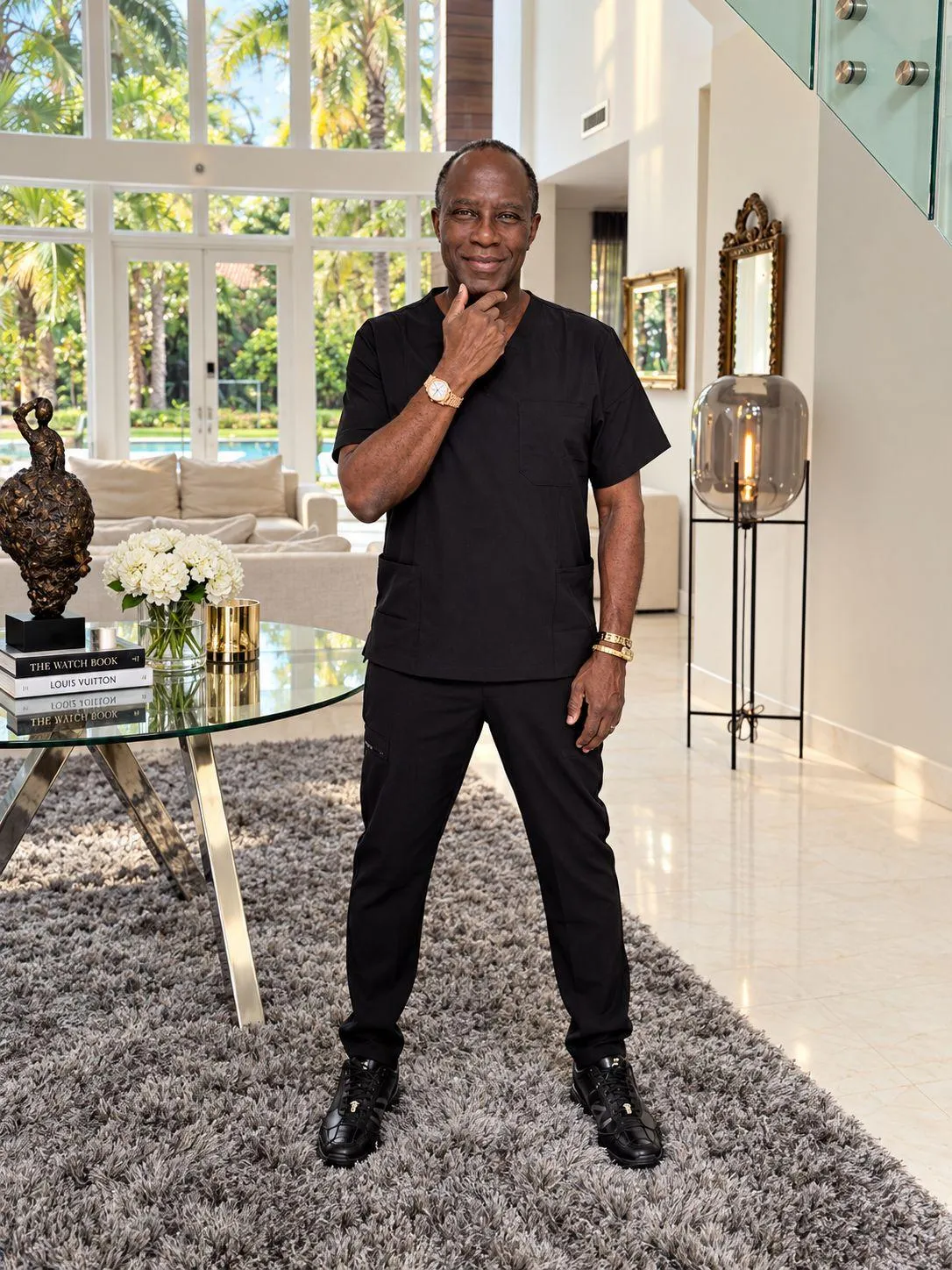 Professor Bankole A. Johnson smiling in a modern hallway, wearing a black shirt and gold jewelry
