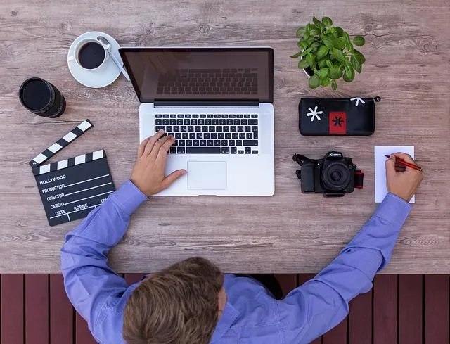 Overhead view of a Man at desk with his computer, camera, film clapper, pen and paper and coffee.