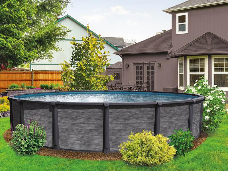 Image d'un modèle de piscine hors-terre en résine . Le mur de la piscine est gris foncé, style pierre, et celle-ci est installée sur un gazon vert avec quelques plantes.