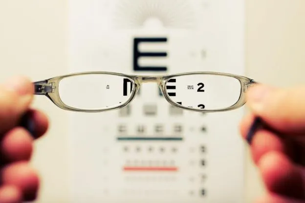 Person holding eyeglass in front of the eye chart