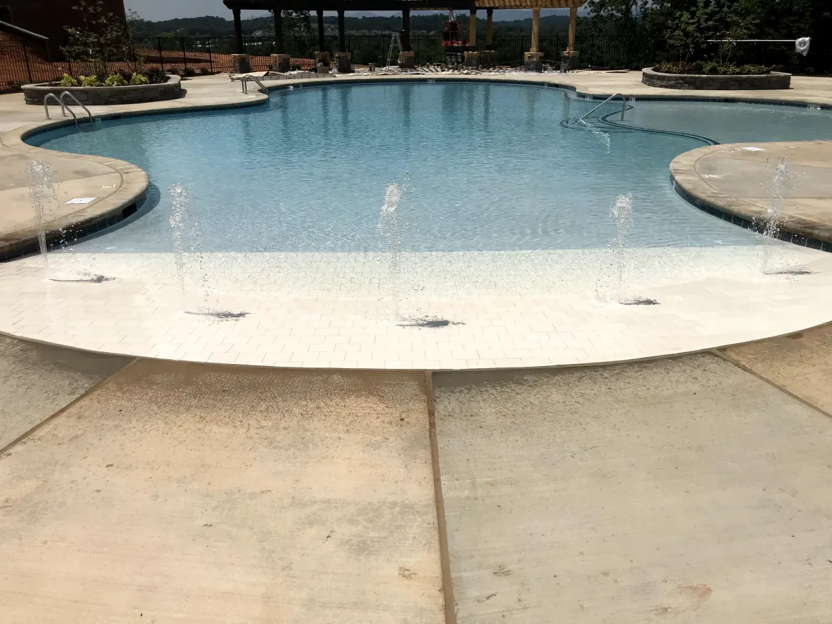 Beach entry pool design with bubblers and commercial Freeform pool extending into the distance.