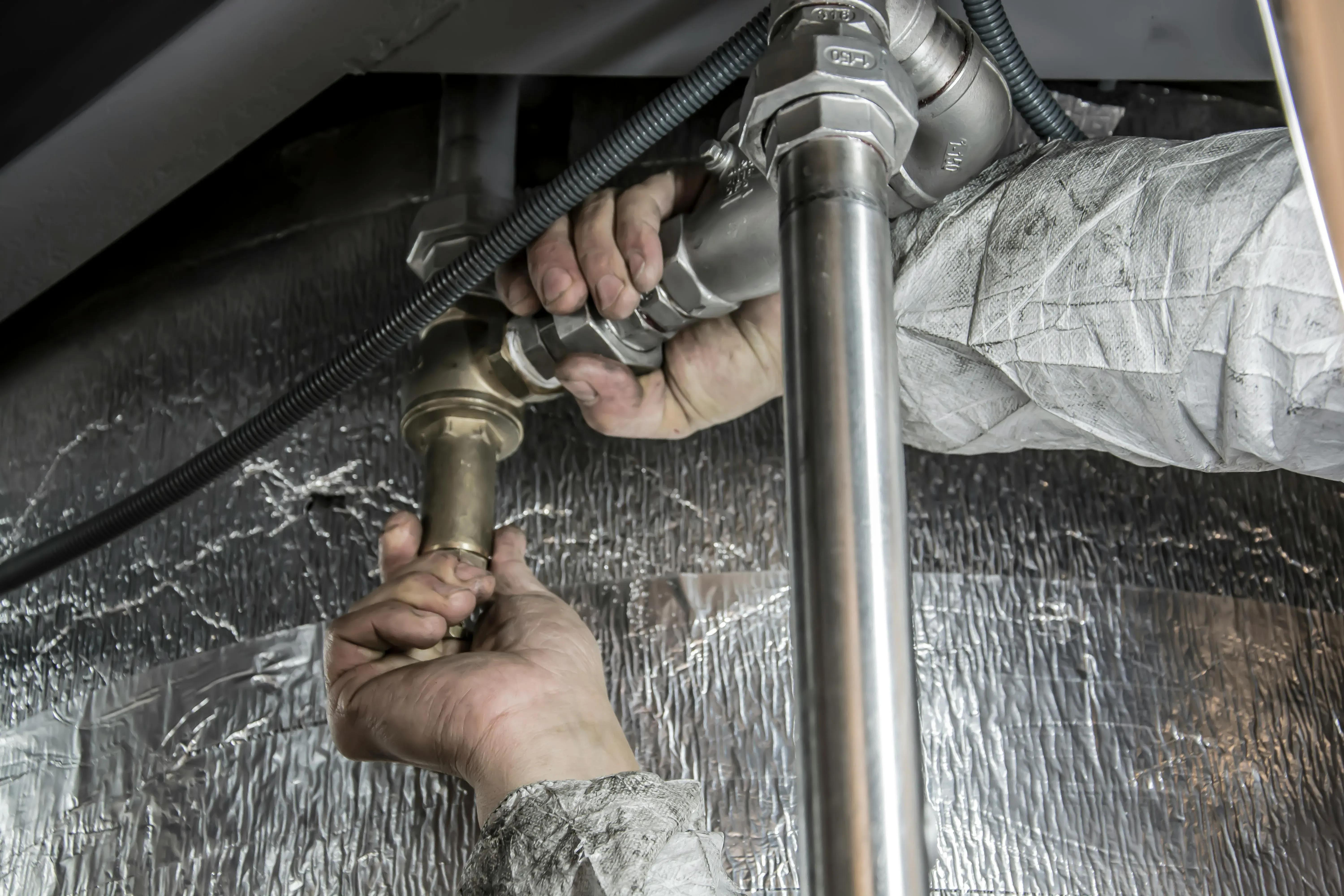 Hands connecting metal pipes in a mechanical setting.