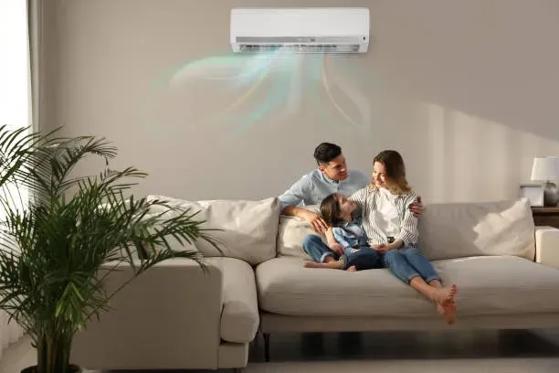Family relaxing under a wall-mounted AC unit, illustrating the comfort benefits of regular HVAC maintenance in summer.