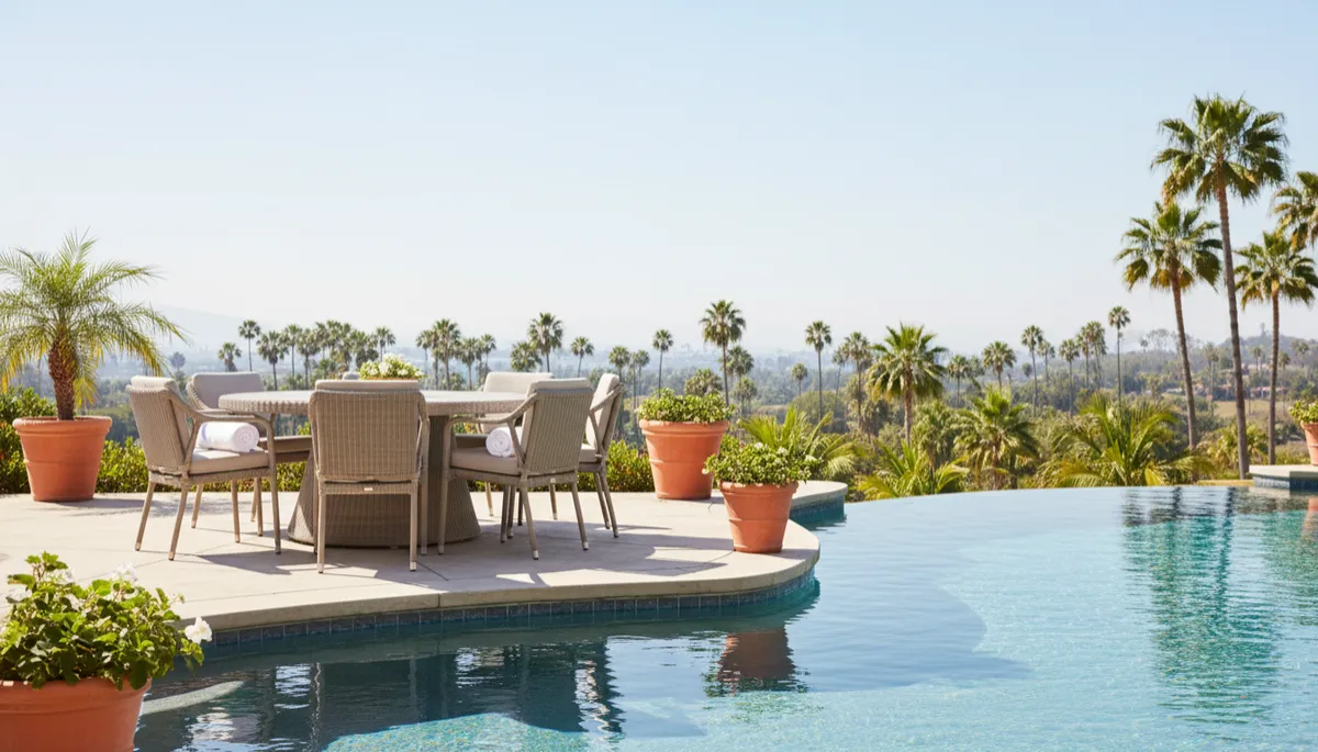 Professionally staged poolside patio with neutral furniture and clear blue water