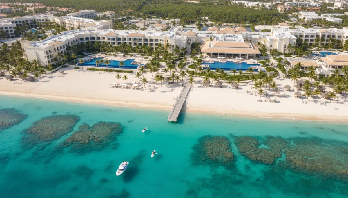 photorealistic aerial view of a luxury beachfront resort in Punta Cana with turquoise water, palm trees, and white sand, bright daylight, clean premium aesthetic