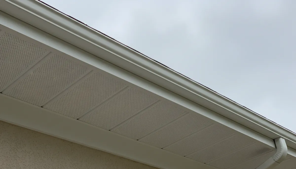 close-up neutral-color photograph of a home’s eaves showing perforated white soffit panels and matching fascia board, shot at an upward angle on an overcast day, realistic detail