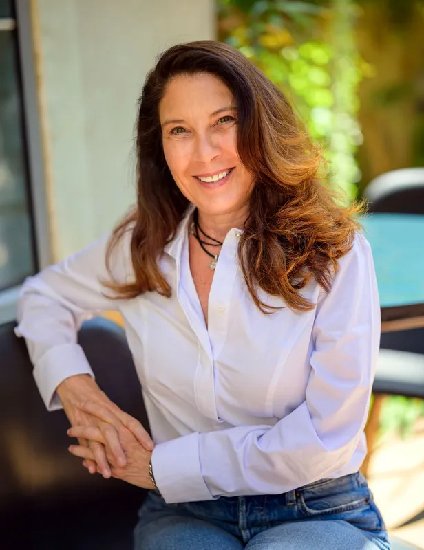 Nicole sitting outdoors in a white blouse and blue jeans