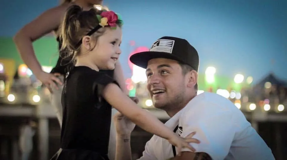 Playful young daughter laughing on father's shoulders at sunset