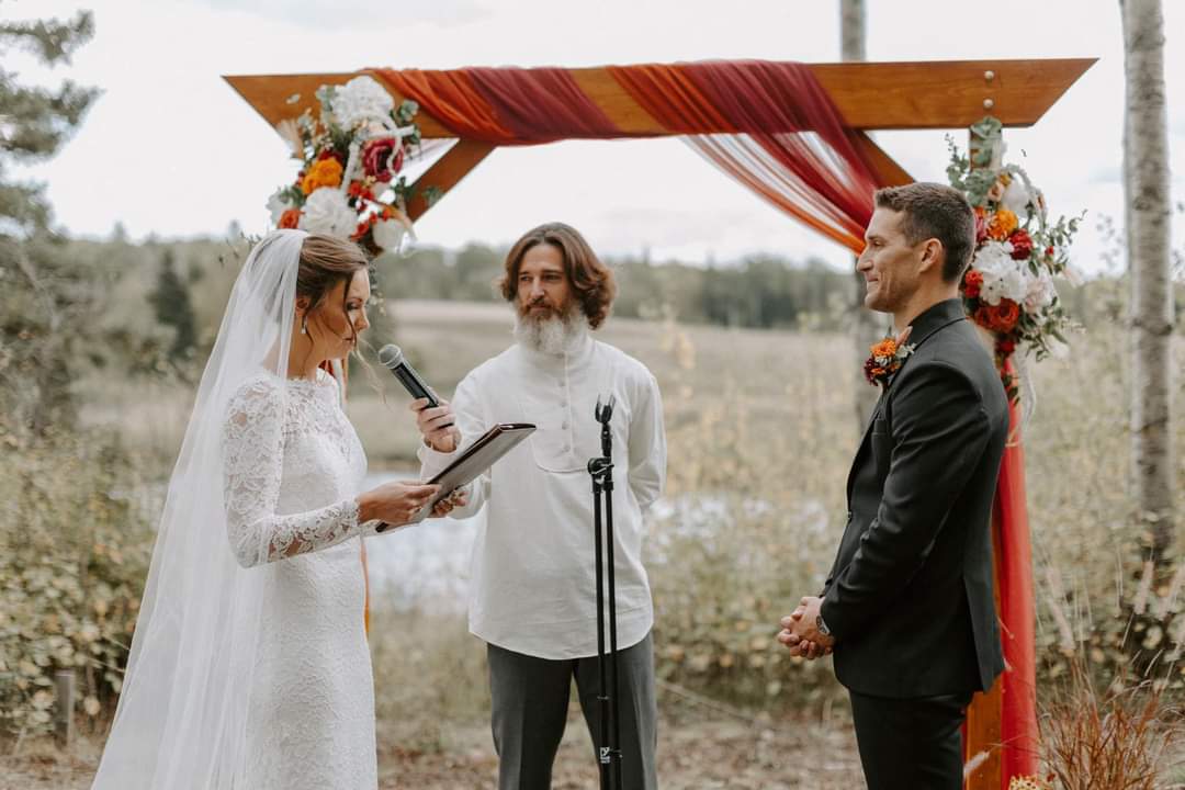 Joseph Ranseth holding a microphone as a bride reads her vows beside the groom.