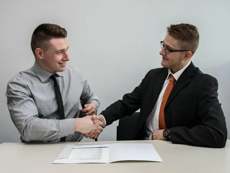 Two men facing each other while shaking hands and smiling