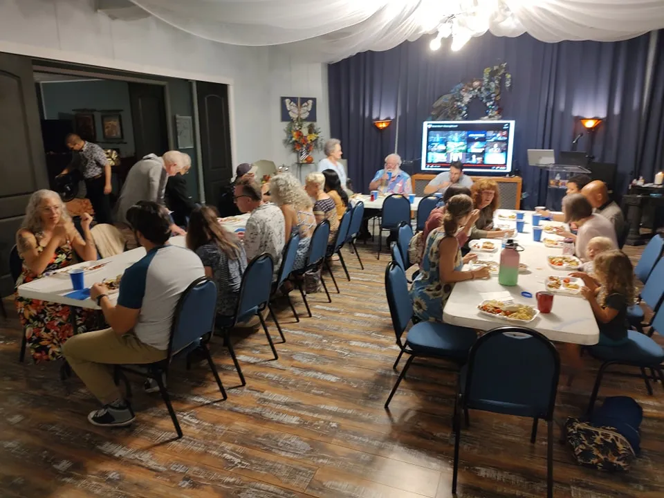 Community members seated at tables enjoying a potluck meal