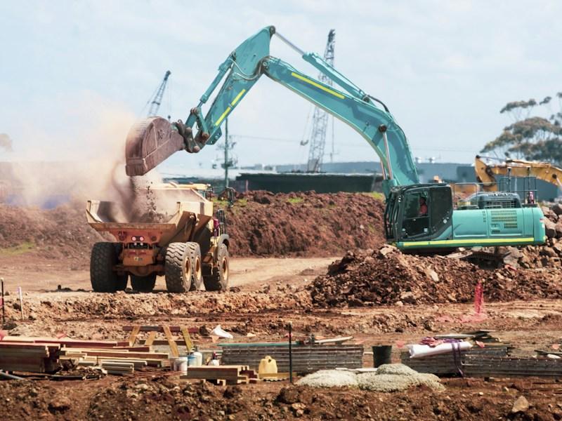 Teal excavator dumping soil into a yellow dump truck at a Fairfax County construction site