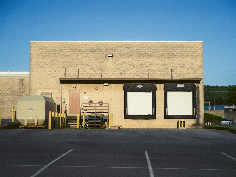 A beige concrete warehouse building with two loading docks and a dumpster