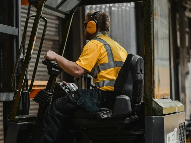 A person in a yellow high-visibility shirt operating a forklift in a warehouse