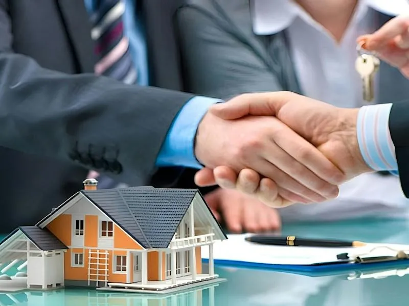 Two men shaking hands over a house model and keys