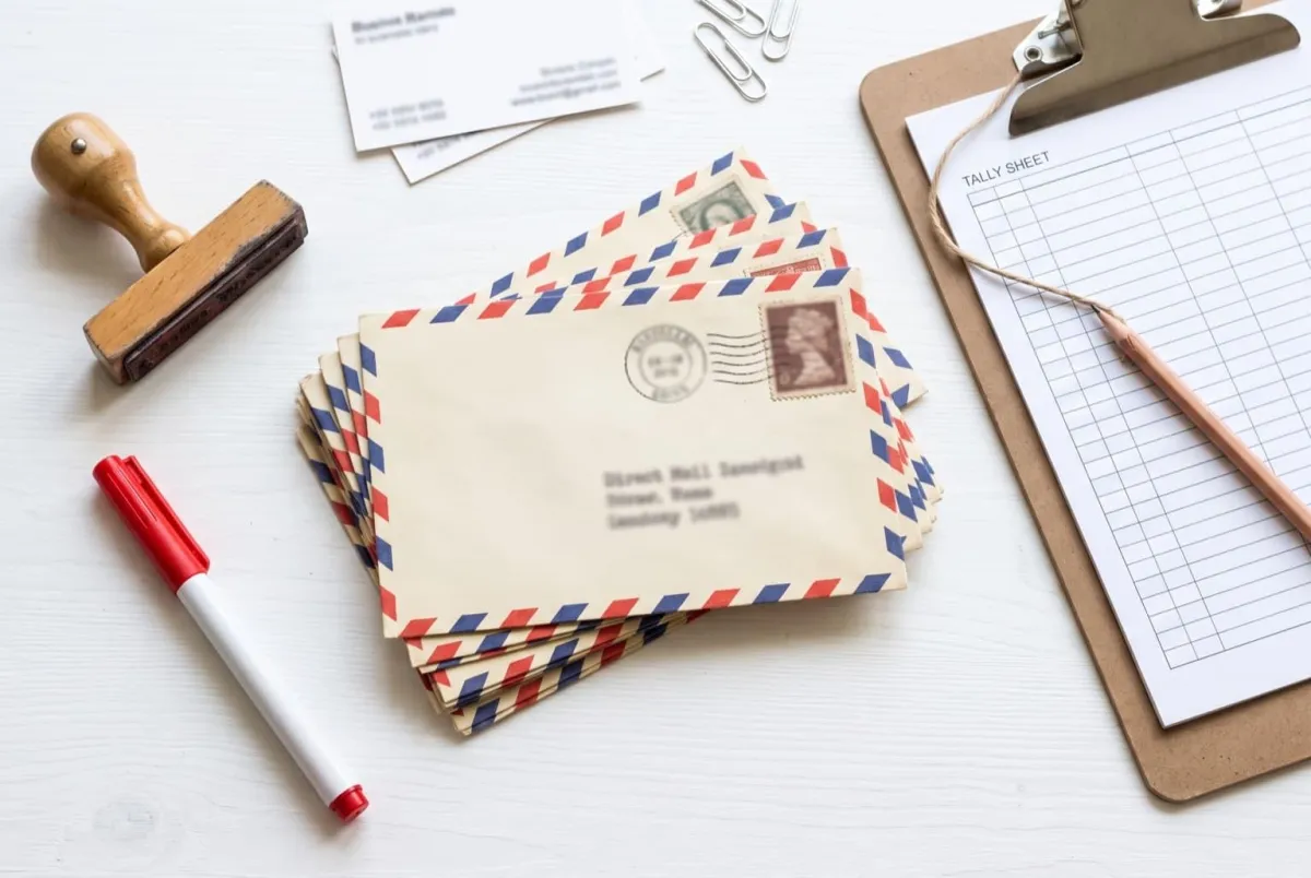 Batch of direct-mail envelopes with stamps beside a clipboard tally sheet