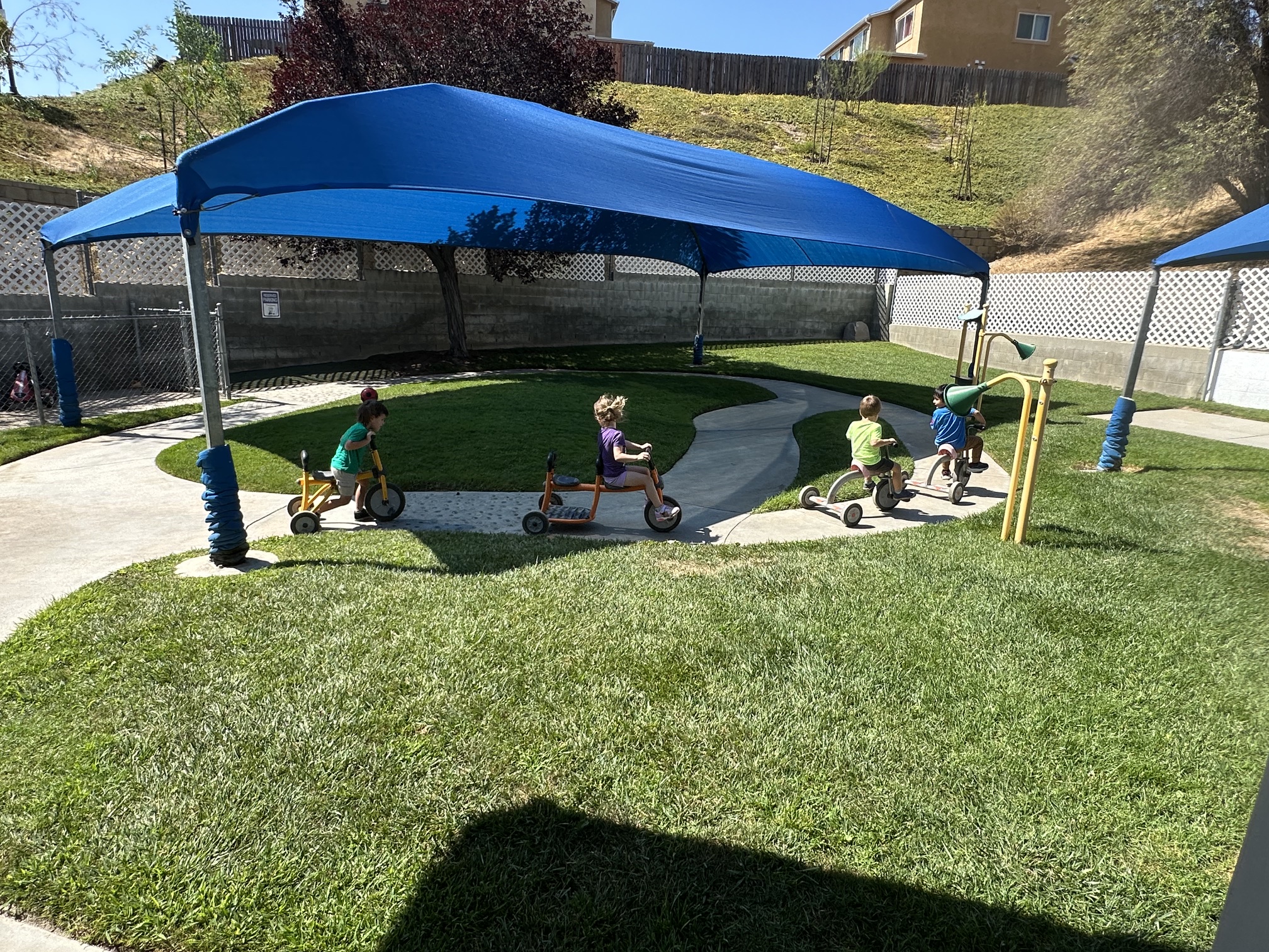 Outdoor grass play area at Creative Years Preschool with children running and playing, wide angle, sunny day