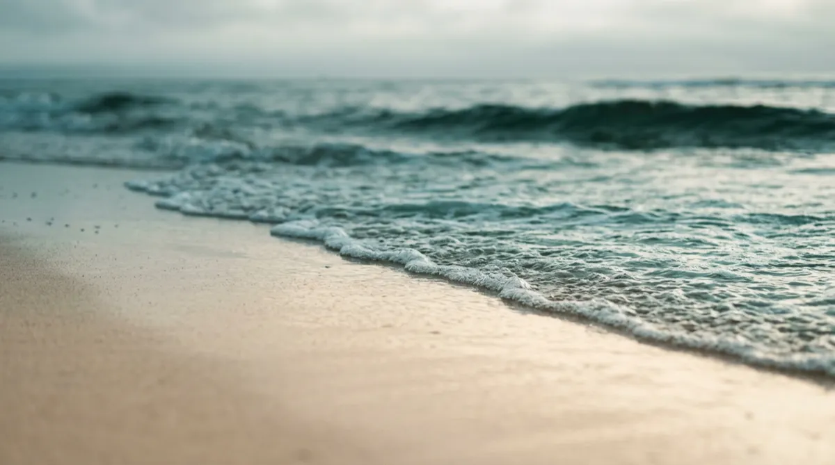 Soft sea-glass teal waves lapping gently against smooth sand along the South Wales coast