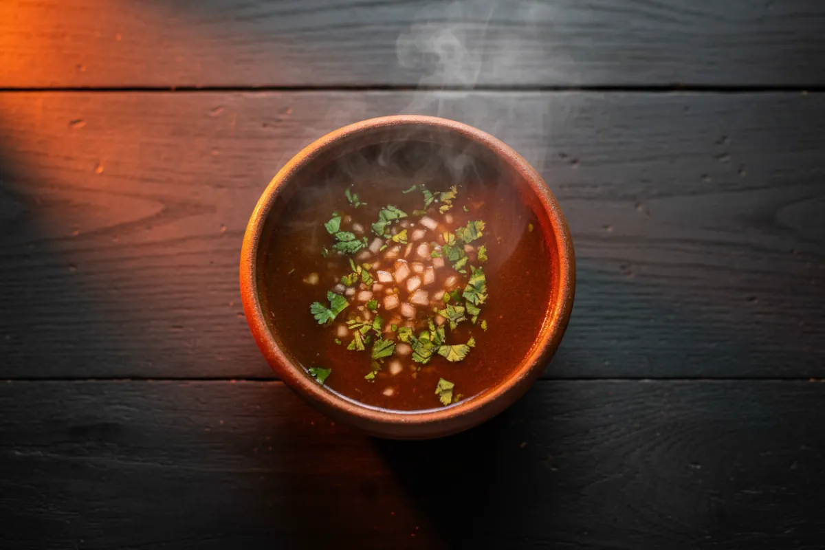 A steaming cup of rich birria consommé