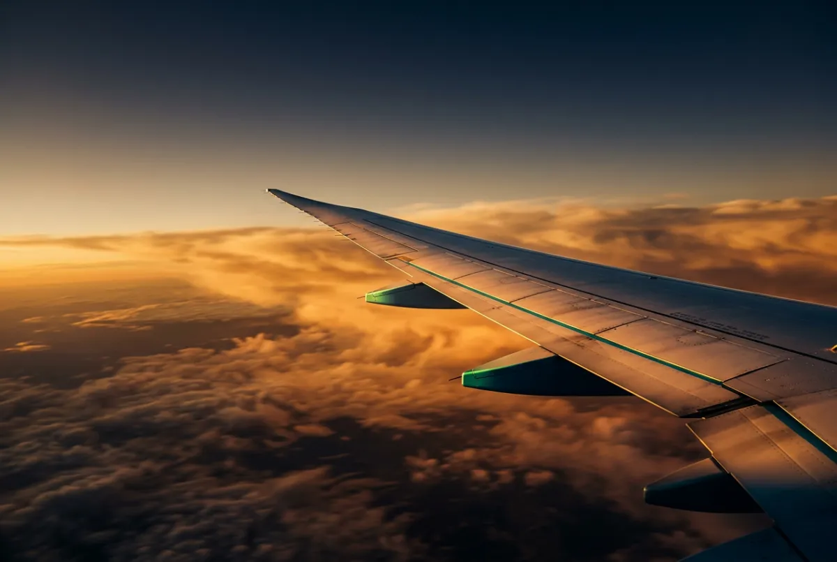 Commercial airplane wing soaring over clouds at sunset