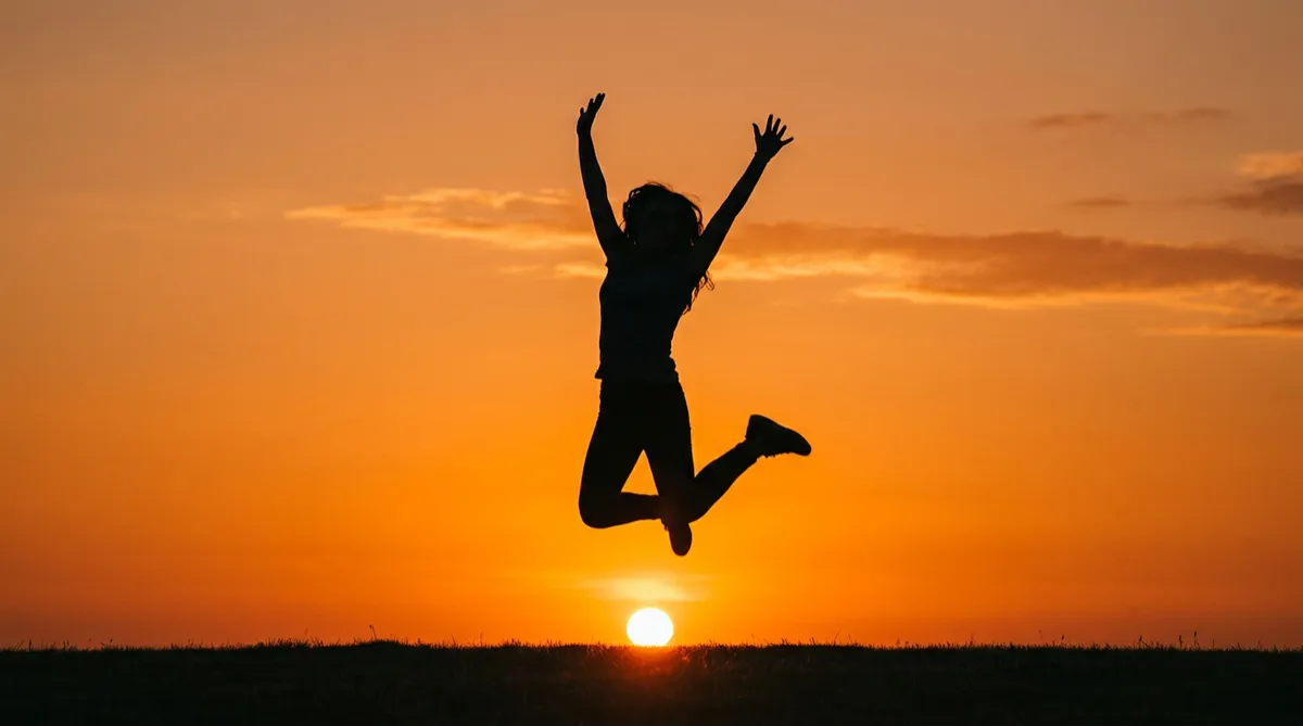 Silhouette of a person jumping excitedly against an orange sunset background