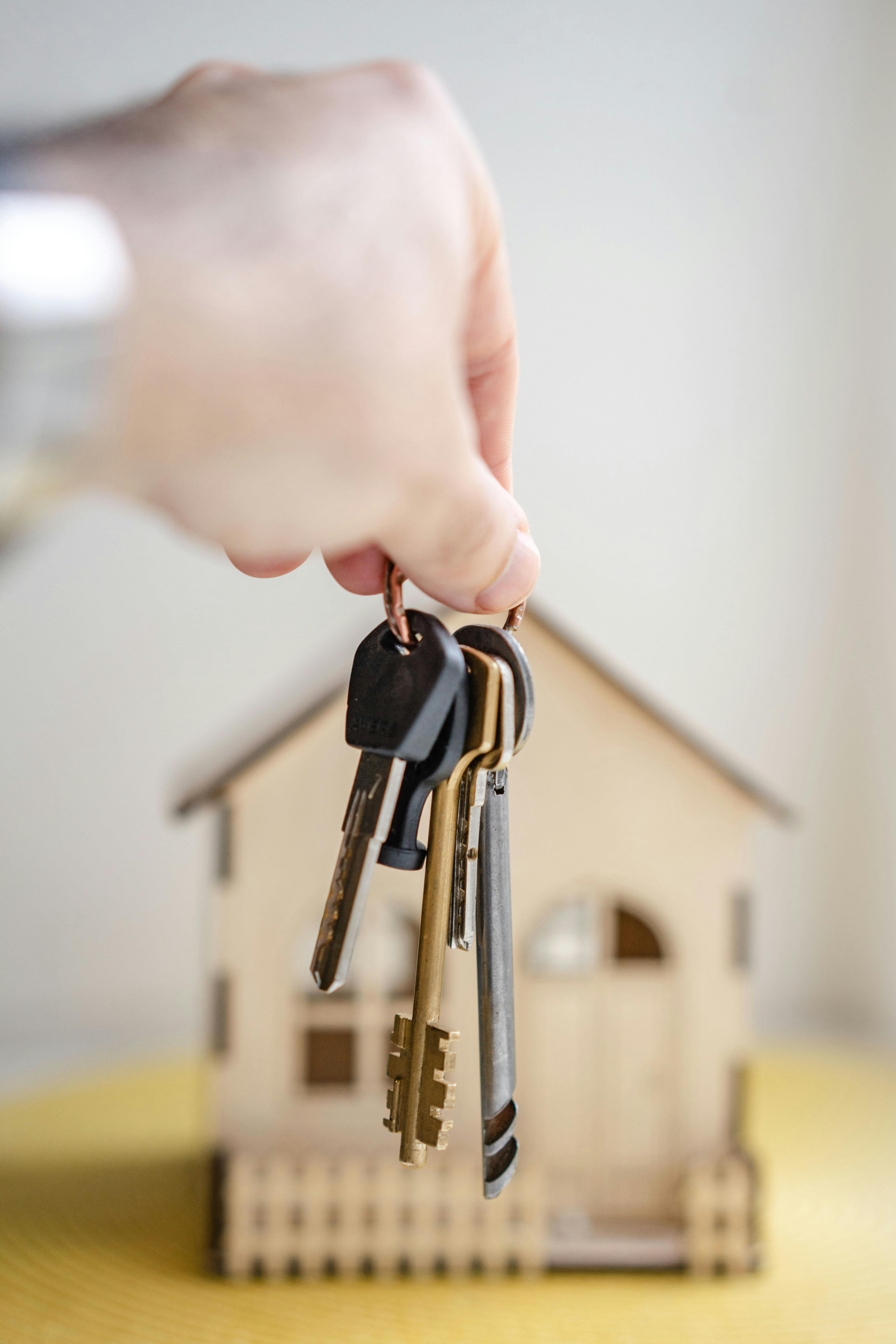 Hands holding house keys over a wooden house model