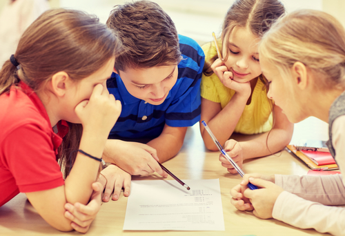 education, elementary school, learning and people concept – group of school kids with pens and papers writing in classroom