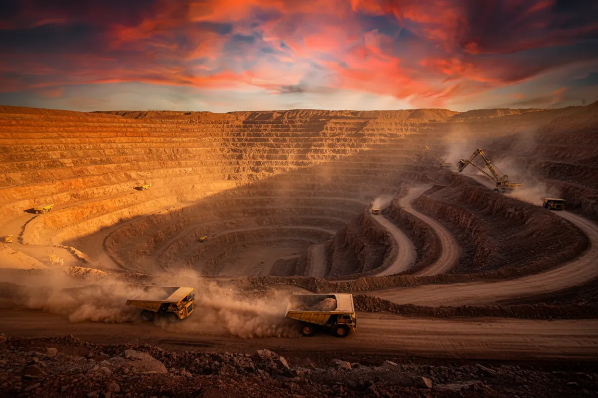 Open pit mining operation with terraced benches, haul trucks, and heavy machinery in a dusty environment