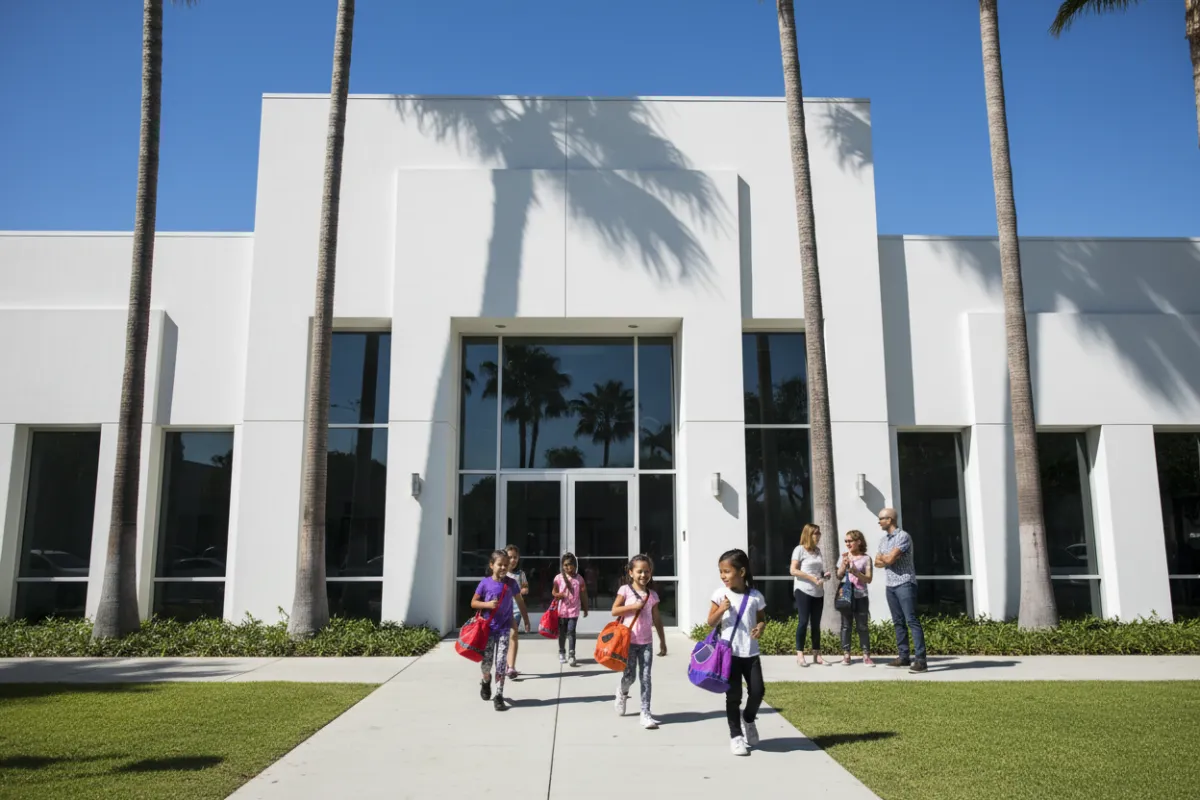 Fullerton studio, white modern exterior, palm trees, children entering with dance bags, parents smiling, 3:2 aspect ratio