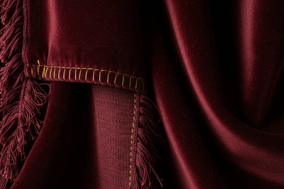 Deep maroon velvet curtain folded with visible pile and stitch detail.