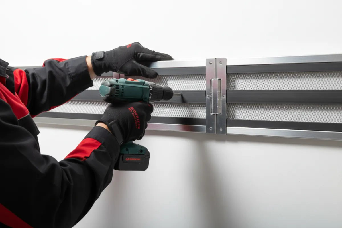 Close-up photo of technician installing pest protection network components; technician uniform black and red
