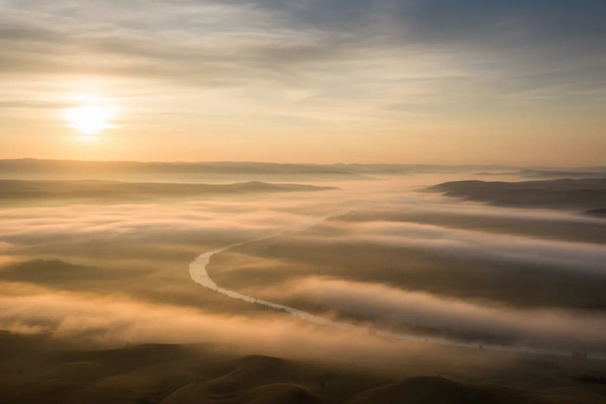 Tranquil sunrise over a misty golden valley, editorial landscape conveying peace and new beginnings