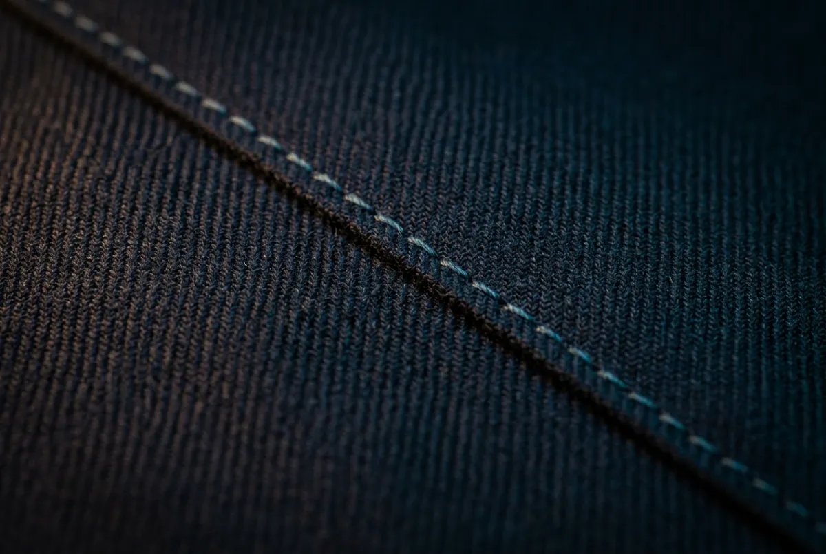Extreme close-up of tailored worsted wool suit fabric with precision hand-stitching detail